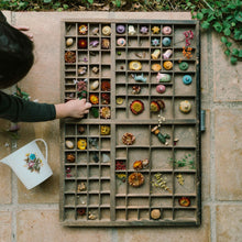 Load image into Gallery viewer, Child interacting with a wooden box containing small decorative items on a stone floor.