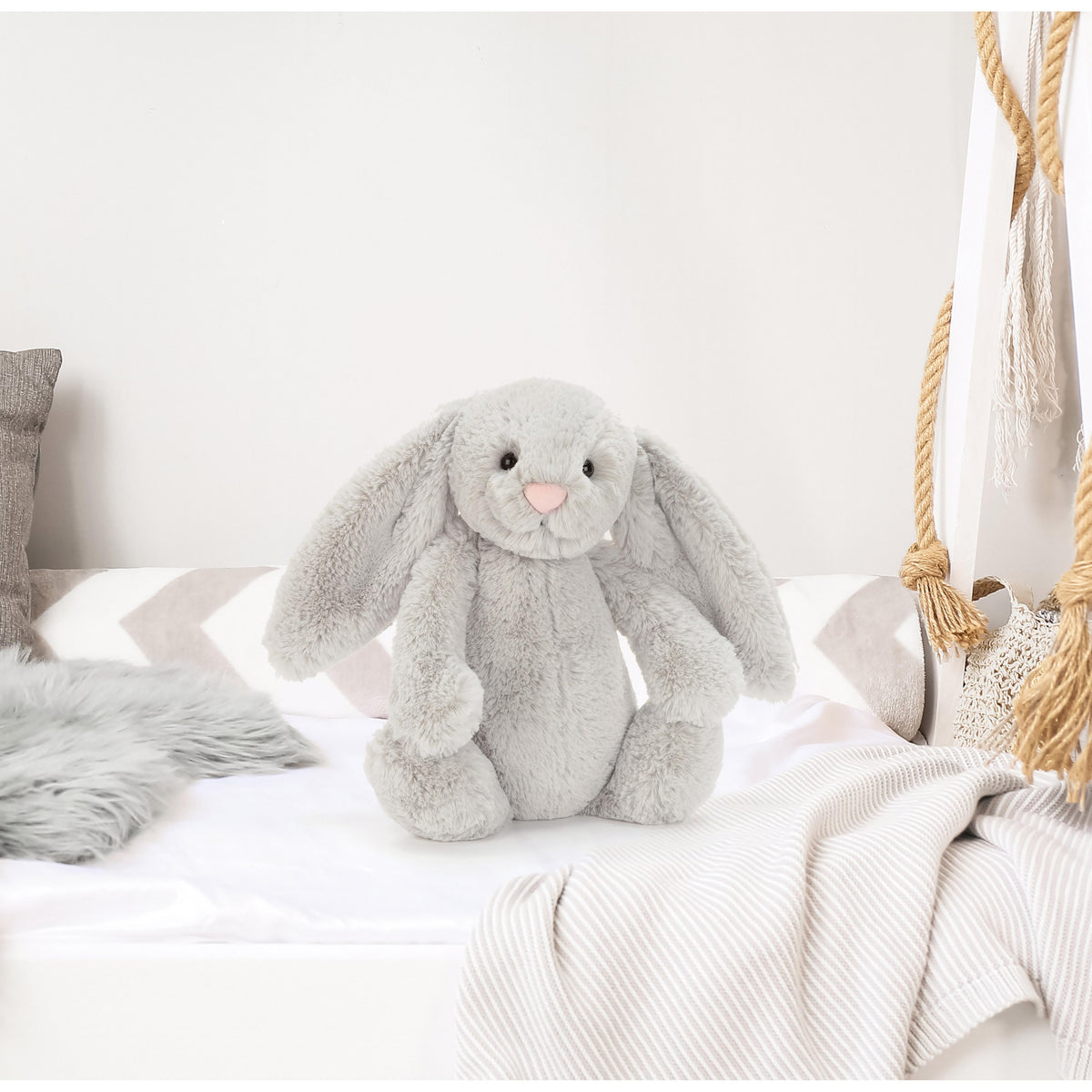 Gray plush bunny toy on a white bed with neutral decor