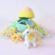 Load image into Gallery viewer, Small unicorn toy with a yellow top and green body rainbow egg, surrounded by colorful string on a light pink background.