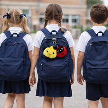 Load image into Gallery viewer, Three children wearing navy blue backpacks with a school building in the background.