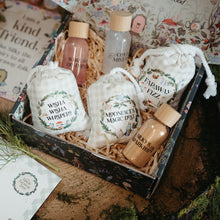Load image into Gallery viewer, A curated gift box set featuring four white muslin drawstring pouches with printed labels, two small bottles with wooden caps, and a decorative box lined with shredded paper, styled on a rustic wooden surface with printed cards and greenery.