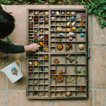 Child interacting with a wooden box containing small decorative items on a stone floor.