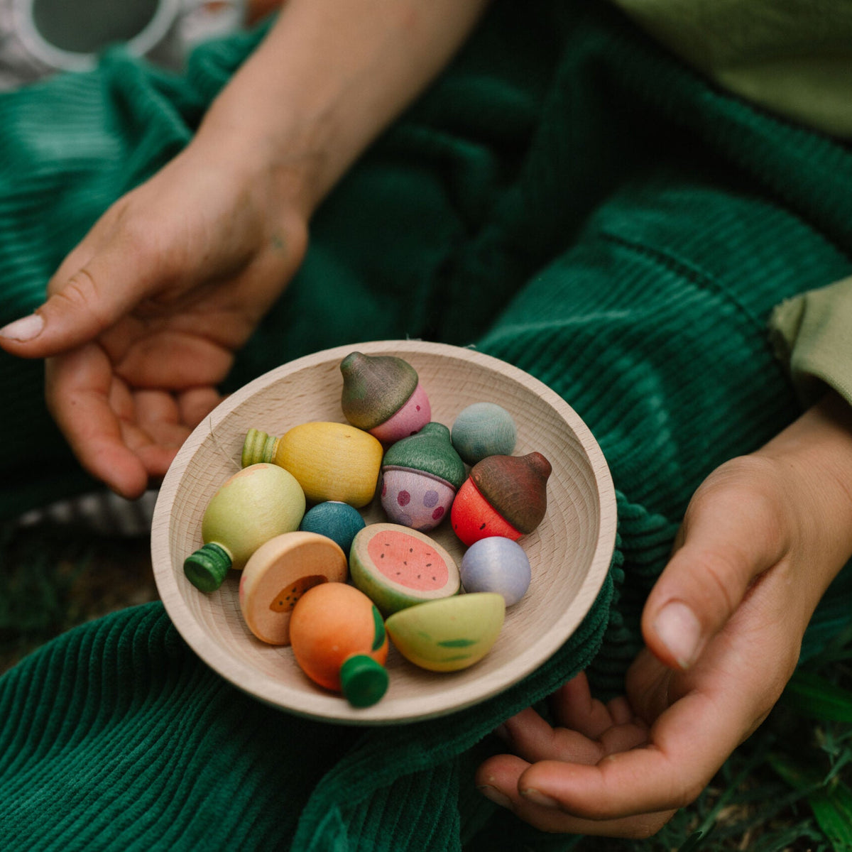 Person holding a bowl of colorful clay figurines in a natural setting.