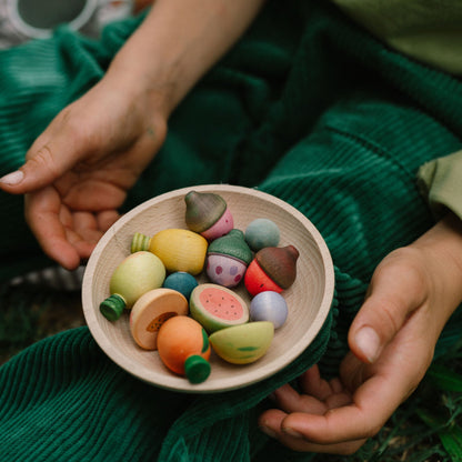 Person holding a bowl of colorful clay figurines in a natural setting.