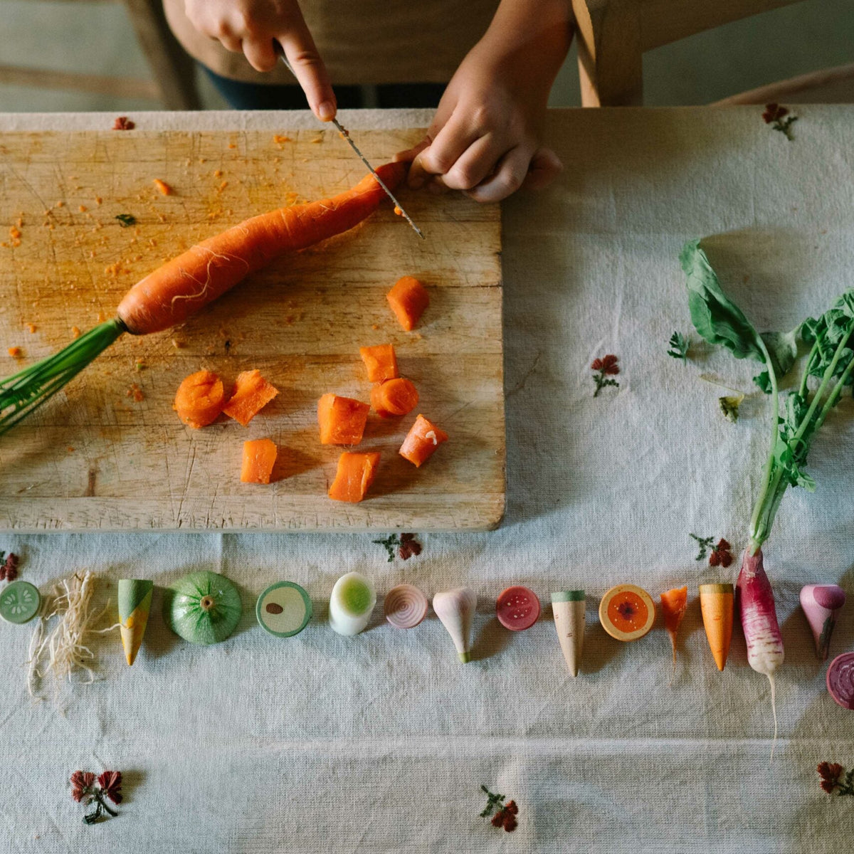 Person cutting a carrot on a wooden cutting board with various vegetables arranged below.
