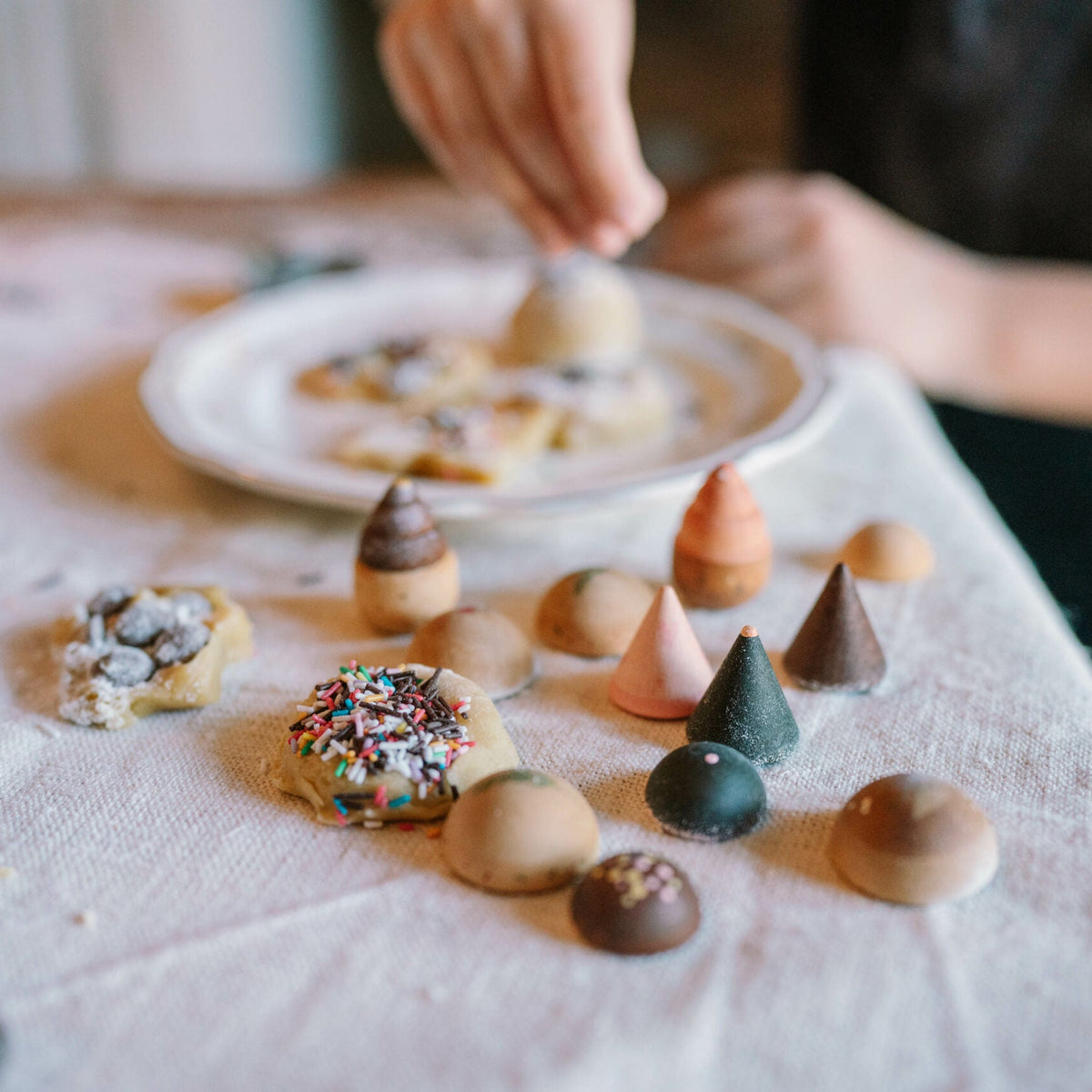 Children's hands arranging small cookies on a tablecloth.