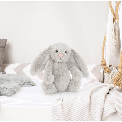 Gray plush bunny toy on a white bed with neutral decor