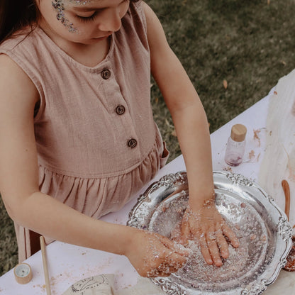 Young girl playing with potions on a silver tray outdoors