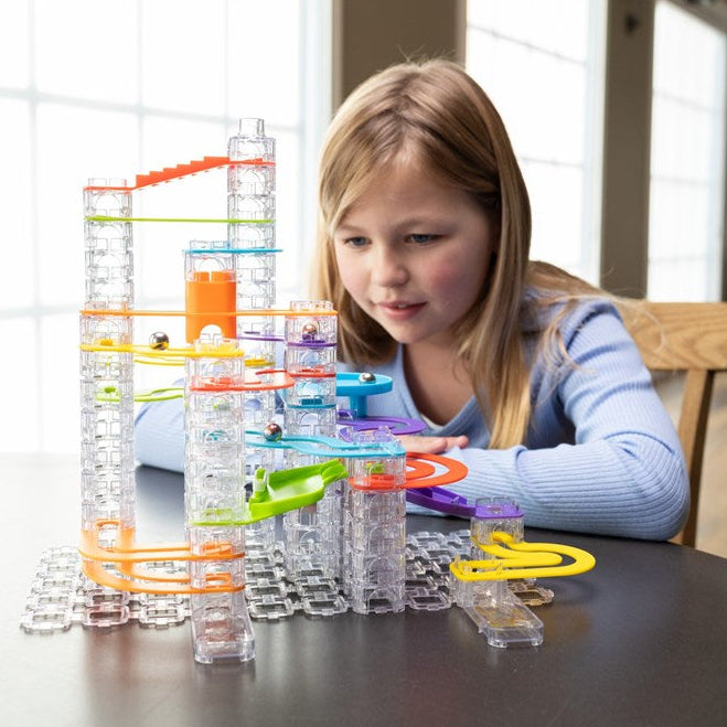 Child playing with a marble run toy set on a table.