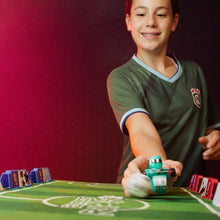 Load image into Gallery viewer, Child playing with a toy Foosbot on a green surface against a red background

