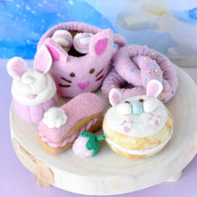 Load image into Gallery viewer, Plush toys shaped like donuts and a bagel on a wooden stand with a colorful background.

