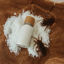 Load image into Gallery viewer, White bottle with a wooden cap on a bed of salt next to spiders on a wooden surface
