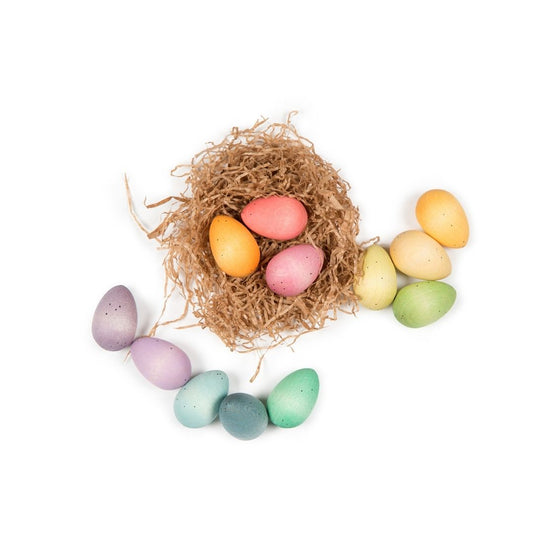 A collection of pastel rainbow-coloured wooden eggs spilling out of a small nest onto a white surface.