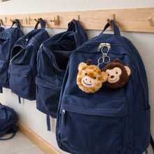 Load image into Gallery viewer, Row of blue backpacks hanging on a rack with plush monkey and giraffe keychains.
