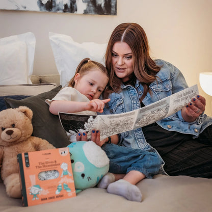 Woman and child telling a story from heydoodle tales on a bed with a teddy bear and plush toy nearby.