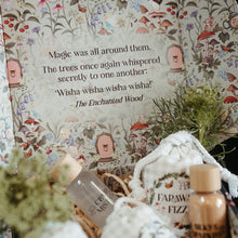 Load image into Gallery viewer, A styled product display featuring a decorative illustrated box lid with a quote from 'The Enchanted Wood,' alongside small bottles and a white drawstring bag labeled 'FAPAW FIZZ' in a rustic, dark setting with dried greenery.
