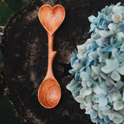 Wooden heart-shaped spoon on a dark surface with blue flowers.