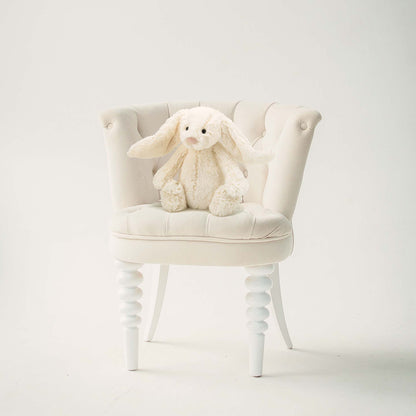 White plush bunny toy on a white chair against a white background