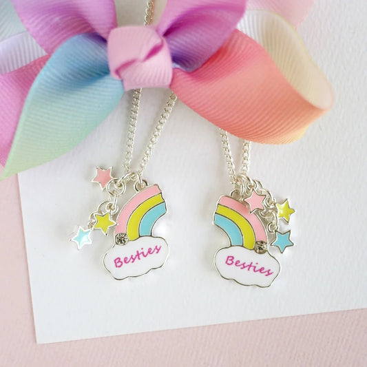 Two silver-plated enamelled half rainbows with star charms on chains, displayed on a white card with a multicolored ribbon above them.